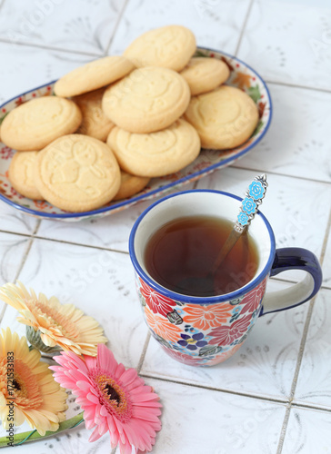 Ceramic mugs with flowers ornament with tea on the kitchen table with cookies on the background. Selective focus. 