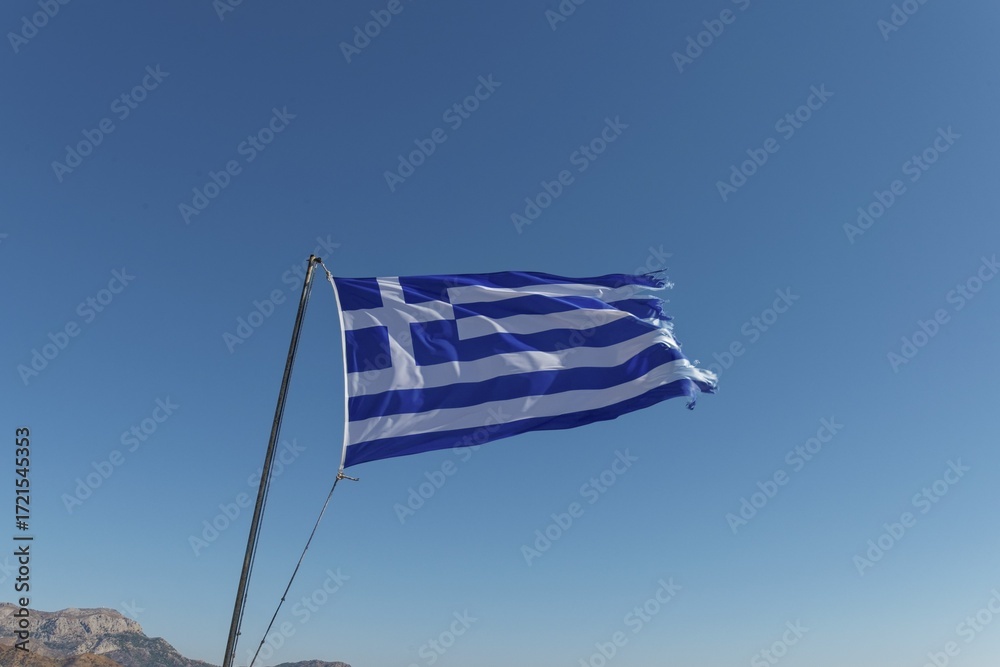 Greek flag waving in the wind against a clear blue sky, Menetes, Karpathos, Greece Greek flag waving in the wind against a clear blue sky, Menetes, Karpathos, Greece