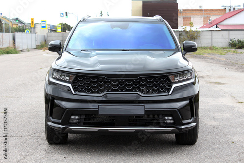 Front view of sleek black SUV with glossy finish, featuring hexagonal grille, sharp LED headlights, and aerodynamic body lines under daylight on paved road. Black modern SUV. Expensive family SUV.