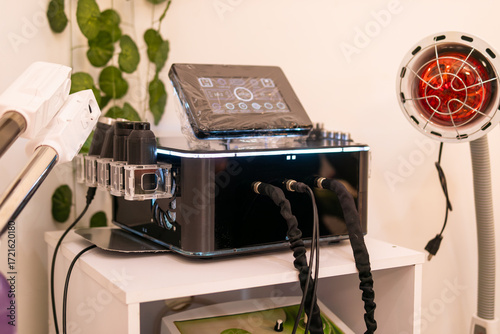 A professional cavitation and radiofrequency machine with a digital screen, multiple applicators, and a red light therapy lamp, used for beauty and body contouring treatments in an aesthetic clinic.