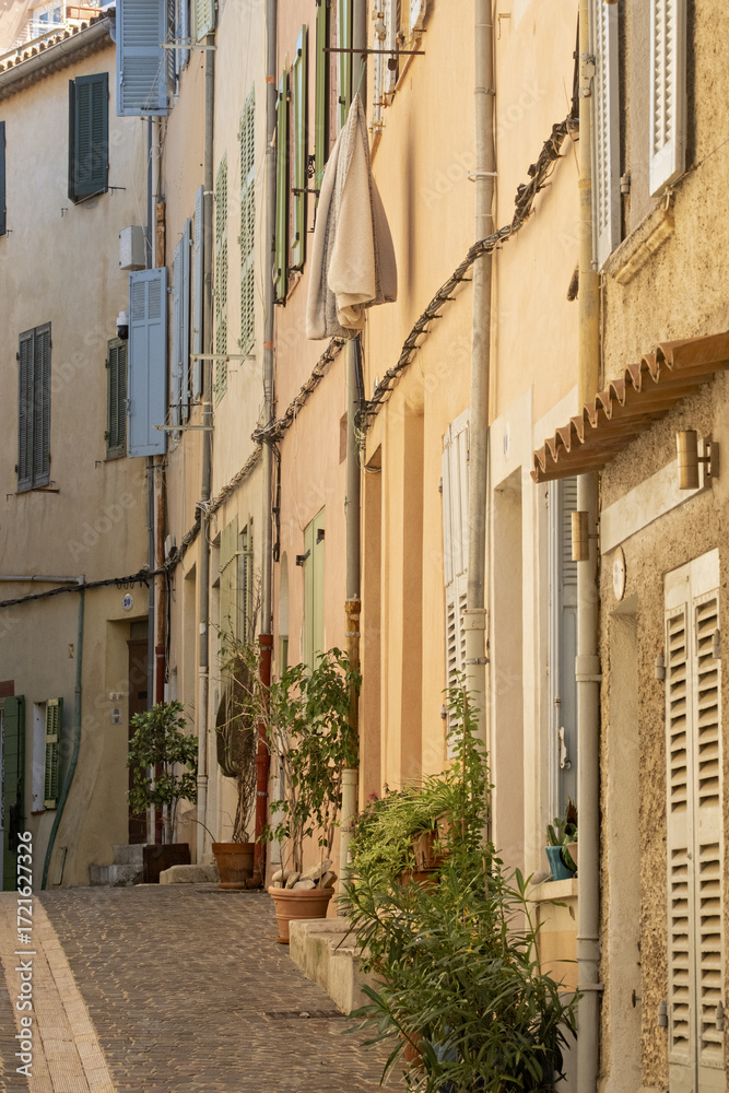 Fototapeta premium beige stone building with multiple shuttered windows. one window has clothes hanging on an outdoor drying rack, including dark-colored pants and shirts in Bandol, Provence, France