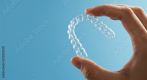 Holding clear aligner for straighter teeth against a bright blue background, demonstrating the latest in orthodontic treatment for a confident smile