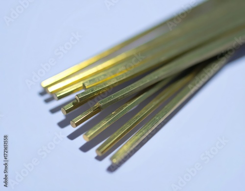 Close up of shiny hexagonal brass rods on light blue surface