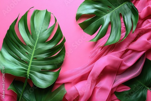 Two monstera leaves and pink fabric lay on a pink background. It is good for tropical backgrounds, banner ads and summer themes.
