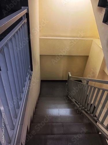 A modern indoor downward staircase with grey metal railing and grey ceramic tiled steps.