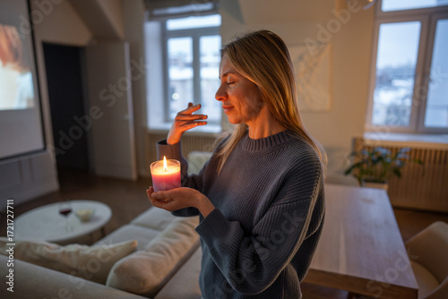 Картината върху платно Happy middle aged woman enjoys lighted aromatic candle in glass filling cozy home with pleasant smell