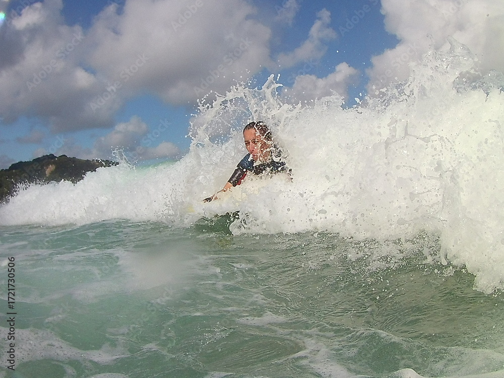 Naklejka premium An energetic photo of a female surfer riding her board through the ocean waves. She is smiling and exudes joy, freedom and passion for water sports. Suitable for topics related to summer, sea,