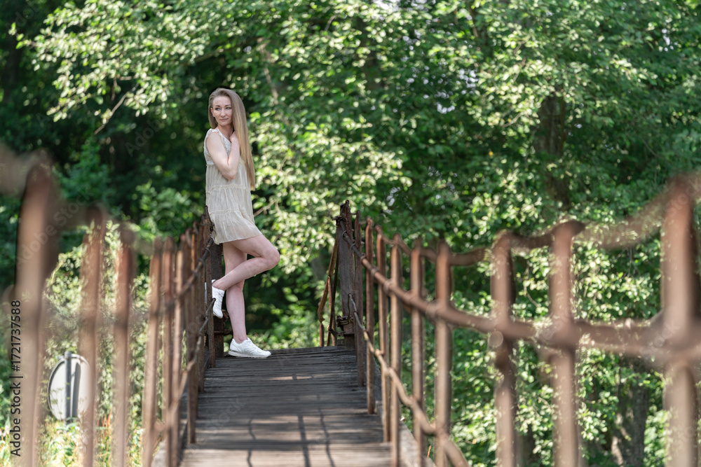 Obraz premium Young Caucasian 20s Woman Standing on a Wooden Bridge in a Lush Forest Setting