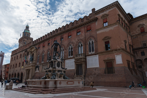Fountain of Neptune in Bologna, Italy, under a bright blue sky dotted with fluffy white clouds