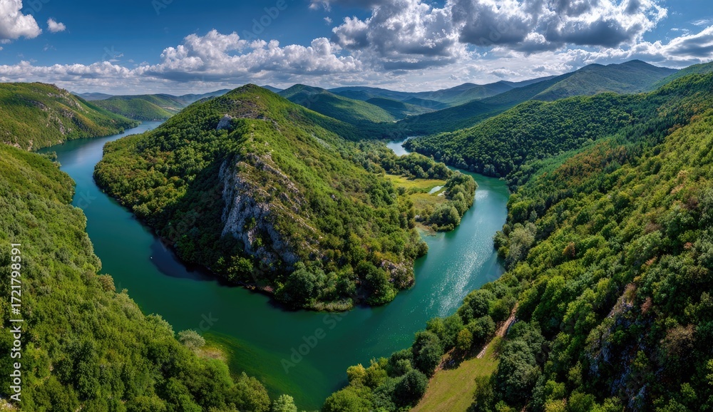 Fototapeta premium Serpentine river meanders through lush green hills and valleys under a partly cloudy sky