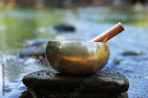 Photography Tibetan singing bowl with mallet on stone near river, closeup