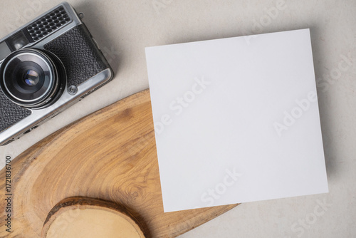 Empty white blank greeting or invitation card, vintage camera and wooden decoration on beige background.
