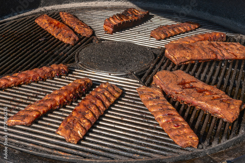 Grilled ribs cooking on round barbecue grill. Delicious barbecue pork ribs with crispy dry rub seasoning placed on circular grill ready for serving.