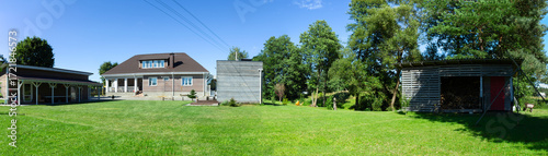 Residential house with porch lawn and wooden structures under clear blue sky. Well maintained countryside home with porch carport and wooden annex ideal for real estate architecture lifestyle.