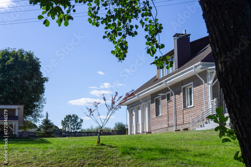 Residential house with porch lawn and wooden structures under clear blue sky. Well maintained countryside home with porch carport and wooden annex ideal for real estate architecture lifestyle.
