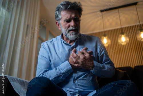 Mature man experiencing sudden chest pain at home, heart attack emergency concept