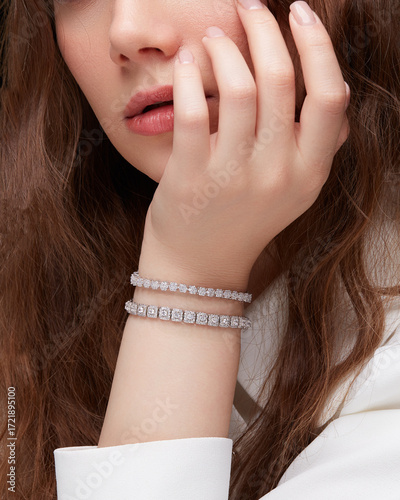 Close-up portrait of woman showing two diamond tennis bracelets on wrist touching face