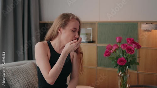 Allergic young woman with hay fever sneezing, coughing because of pollen from a bouquet of pink roses, experiencing strong allergic reaction, suffering from allergy attack, seasonal allergy struggling