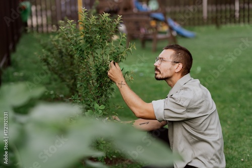 A 35-year-old man works in his garden, tending to plants in natural sunlight. Authentic, unaltered photography capturing the real joy of gardening and connection with nature