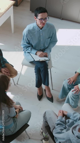 Vertical high angle shot of female counselor giving high-five to all participants of group school therapy session