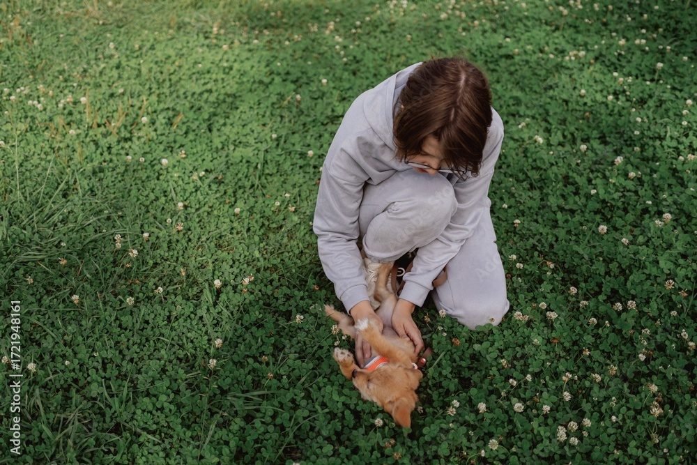 Fototapeta premium A young woman walks her playful puppy in a sunny garden, sharing a tender moment of love and care. Authentic, unaltered photography capturing the special bond between human and pet