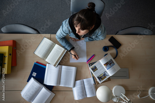 Female student  studying in library and writing notes. Top view of working space with books and notes.