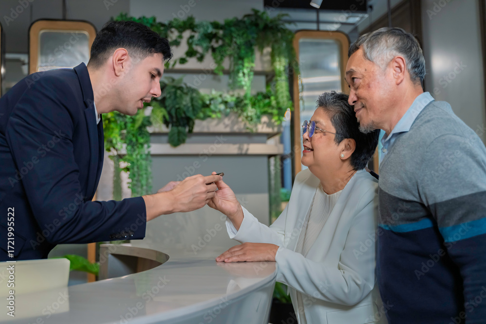 Obraz premium Friendly concierge assisting senior couple at modern hotel reception desk, providing direction with warm service and welcoming hospitality in a stylish urban environment.