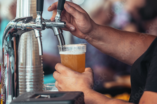 Close-up of a bartender pouring fresh draft beer into a plastic cup at an outdoor festival. Cold foamy lager being served from a tap, symbolizing refreshment, brewing and celebration