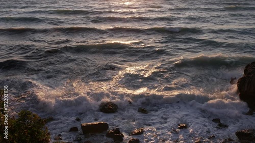 Foamy Waves Crashing Against Coastal Rocks at Sunset on a Slightly Rough Sea