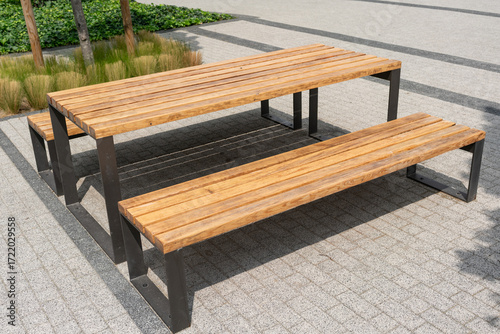Wooden table with benches in modern urban square. Concept of social interaction, community connection, and functional public design in everyday city environment.