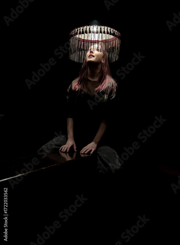 Creative portrait of teenager girl under vintage lampshade with dramatic lighting in dark room