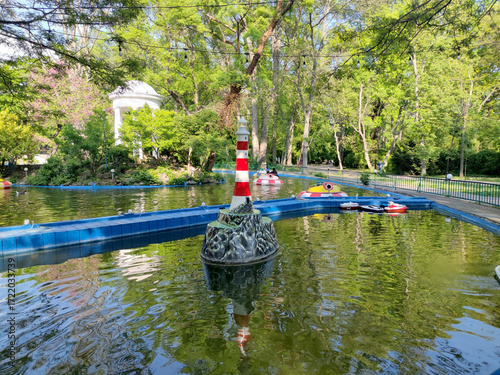 Amusement park pond with boats and small lighthouse in green summer park