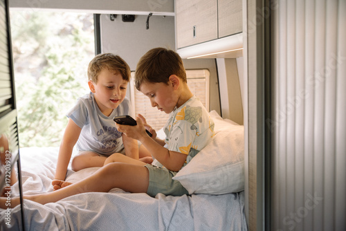 Two boys using smartphone on bed inside camper van