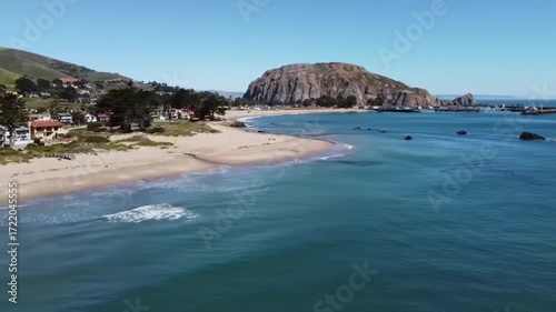 Panoramic coastal scene showcasing a sandy beach, serene ocean waters, and a picturesque hillside town.