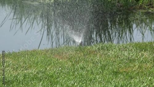 Shooting with a Sprinkler Watering Green Grass in a Public Park on a Sunny Day