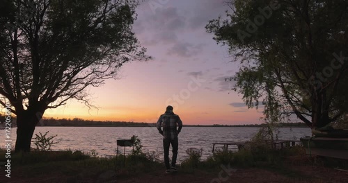 A man stands near river and watching at the beautiful sunset