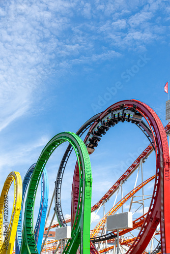 Colorful roller coaster loops in Prater Vienna summer, riders upside down enjoying thrilling amusement park adventure under clear blue sky.