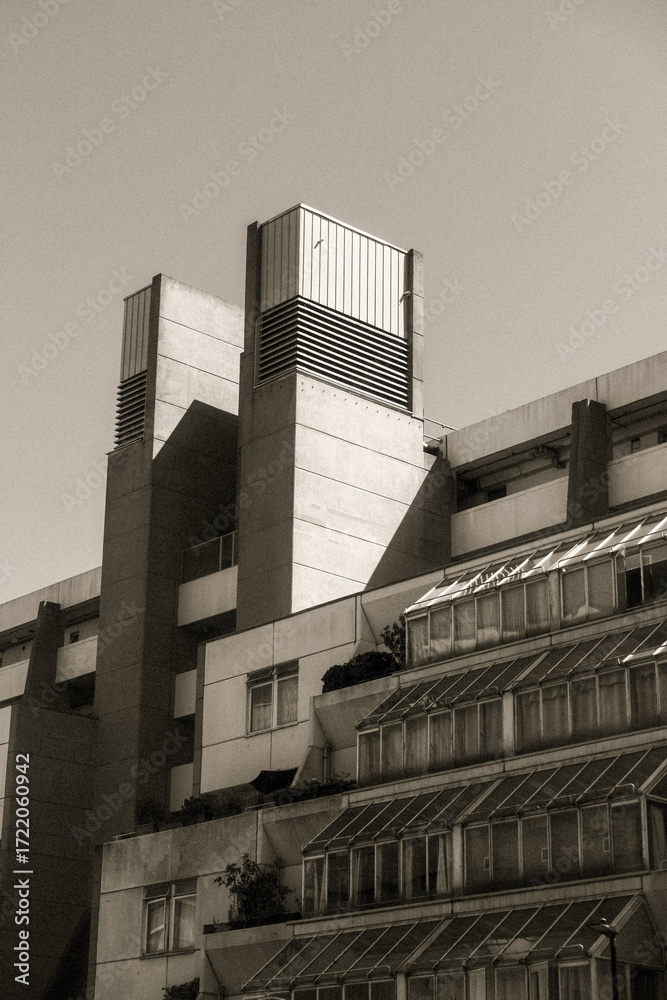 Obraz premium Brutalist concrete building with tiered glass sections in sepia.