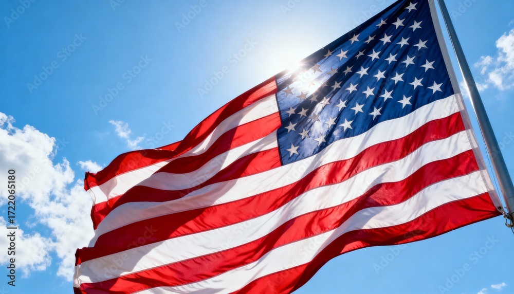 Fototapeta premium Low-angle view of large US flag waving under bright sky, emphasizing patriotism and grandeur
