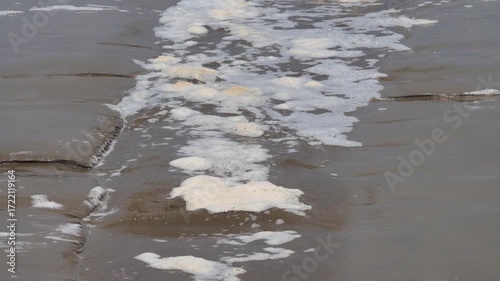 Rapid ebb, falling tide in flakes of foam from washed away organic matter on supralittoral sand coast of the South China Sea. Drain from a littoral bath. Borneo Island
