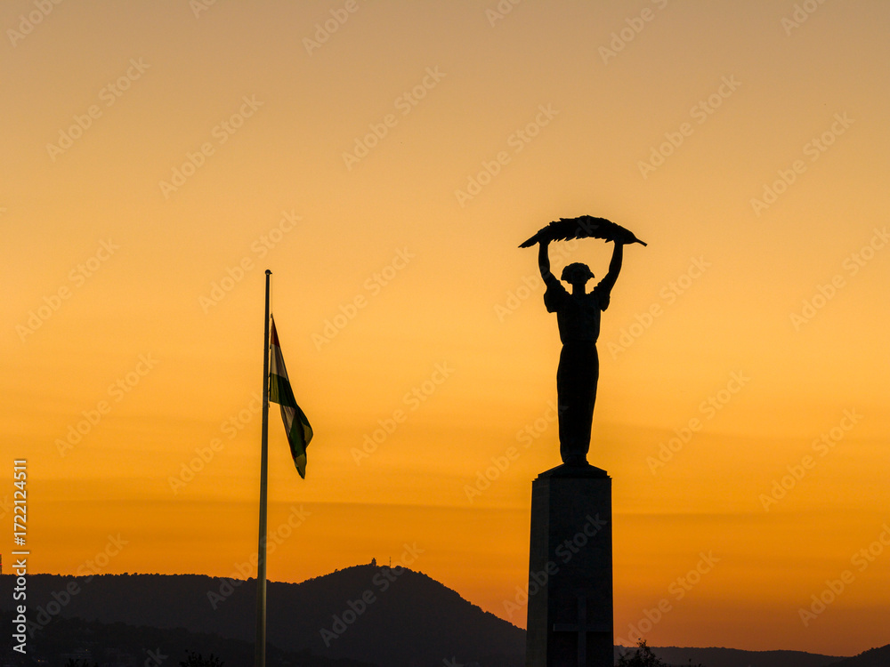 Fototapeta premium The Hungarian flag and Liberty statue's shape on the orange sunset lights in Budapest city. Capital of Hungary