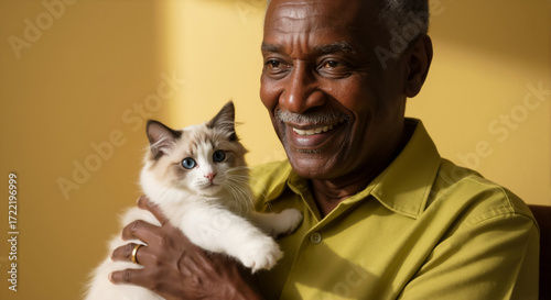 Smiling senior african american man holding a cute ragdoll kitten. Elderly black person with a fluffy cat with blue eyes. Pet owner concept.
