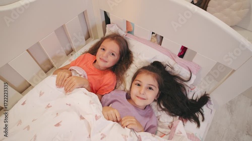 Two sisters happily lying in a cozy bed together, enjoying bedtime in a bright children s room