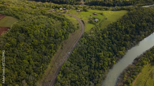 Car driving on a road between green fields, forests and a river. 4K. Aerial. Drone.
