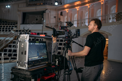 The director of photography with a camera on the set. A professional videographer is working on filming a movie or commercial for a TV series. The filming process takes place indoors in a studio.