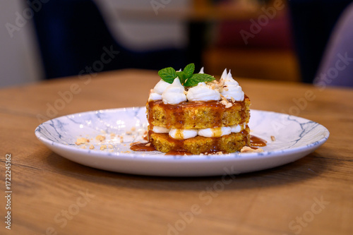 Gourmet dessert with caramel, nuts, sponge cake, and whipped cream on a marble plate, served on a rustic wooden table in fine dining restaurant setting.