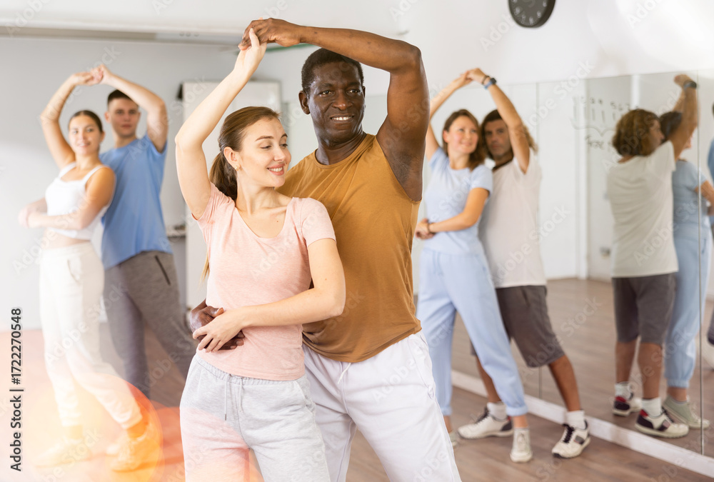 Naklejka premium Joyful active adult men and women learning to dance in pairs in modern choreographic studio, indoors