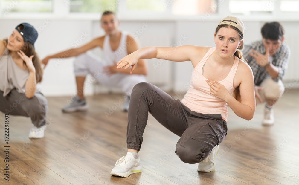 Fototapeta premium Active young girl performing seated pose of breakdance in training hall during dancing classes