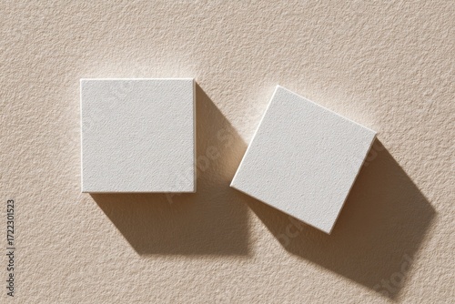 Two blank, square, off-white boxes on a light beige surface, casting shadows