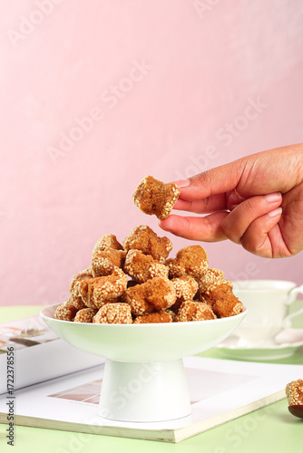Hand Picking Crispy Sesame Fried Snack Balls from Bowl on Pink Background